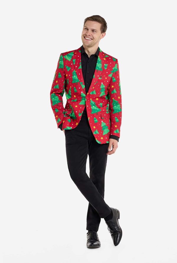 Mann trägt einen roten Weihnachtsblazer mit Weihnachtsbäumen und Sternen. Außerdem trägt er eine schwarze Hose und ein schwarzes Hemd. Ganzkörperbild.
