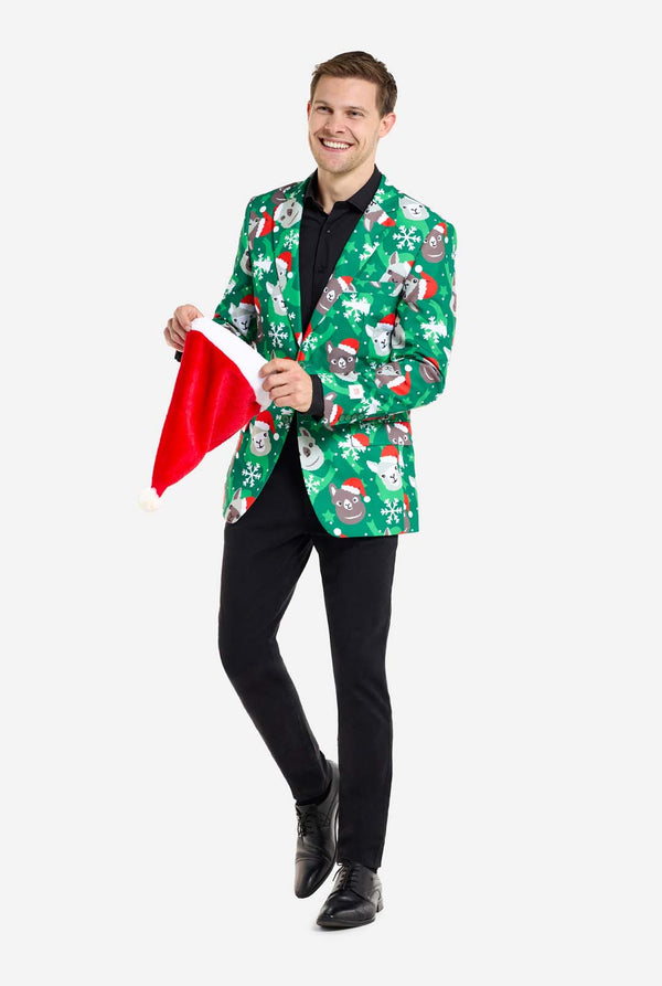 Mann trägt grünen Weihnachtsblazer für Männer mit Weihnachtslamas. Mann trägt außerdem schwarze Hosen und ein schwarzes Herrenhemd. Hält Weihnachtsmütze.
