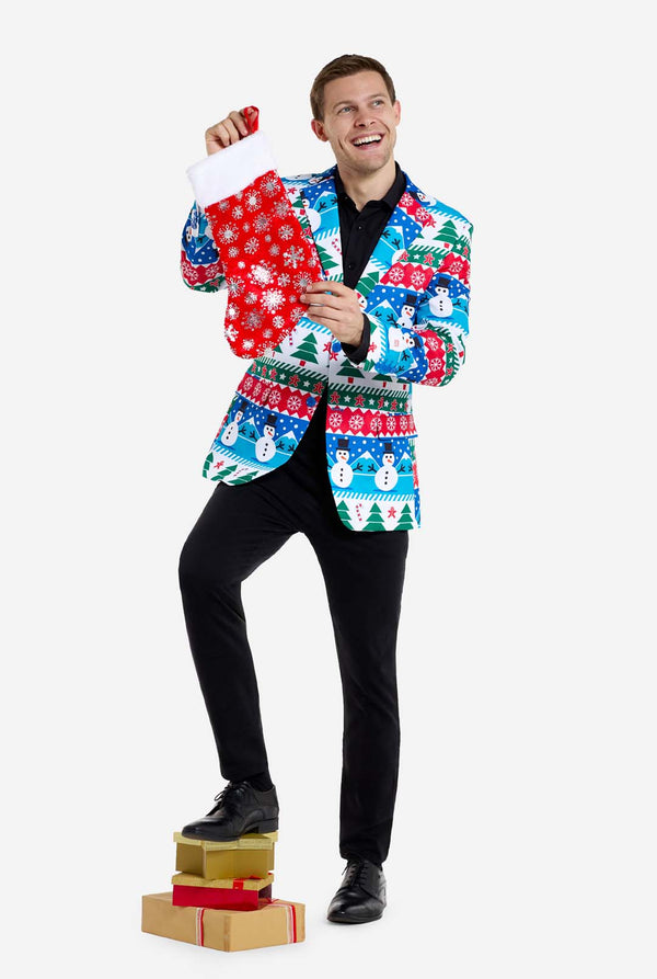 Mann trägt Weihnachtsblazer für Männer mit weihnachtlichen Winterfiguren. Er trägt außerdem eine schwarze Hose und ein schwarzes Herrenhemd. Er hält eine Weihnachtssocke.
