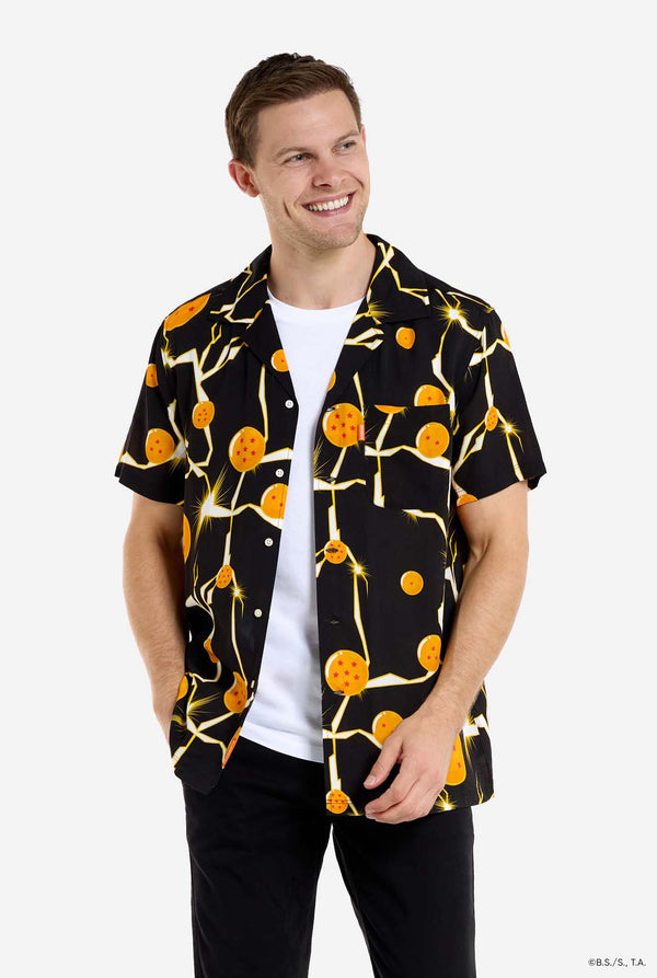 Mann trägt ein schwarzes Hawaiihemd mit Dragon Ball Z-Aufdruck, auf dem Dragon Balls und Lichter zu sehen sind. Außerdem trägt er ein weißes T-Shirt und eine schwarze Hose.