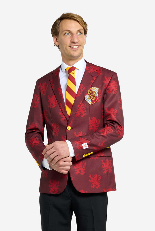 Bild mit hellgrauem Hintergrund und einem Mann, der einen Harry-Potter-Anzug im Gryffindor-Stil trägt. Der Anzug besteht aus einem roten Blazer mit Gryffindor-Logo und hellrotem Löwen-Allover-Print, schwarzen Hosen und einer rot-gelb diagonal gestreiften Krawatte.