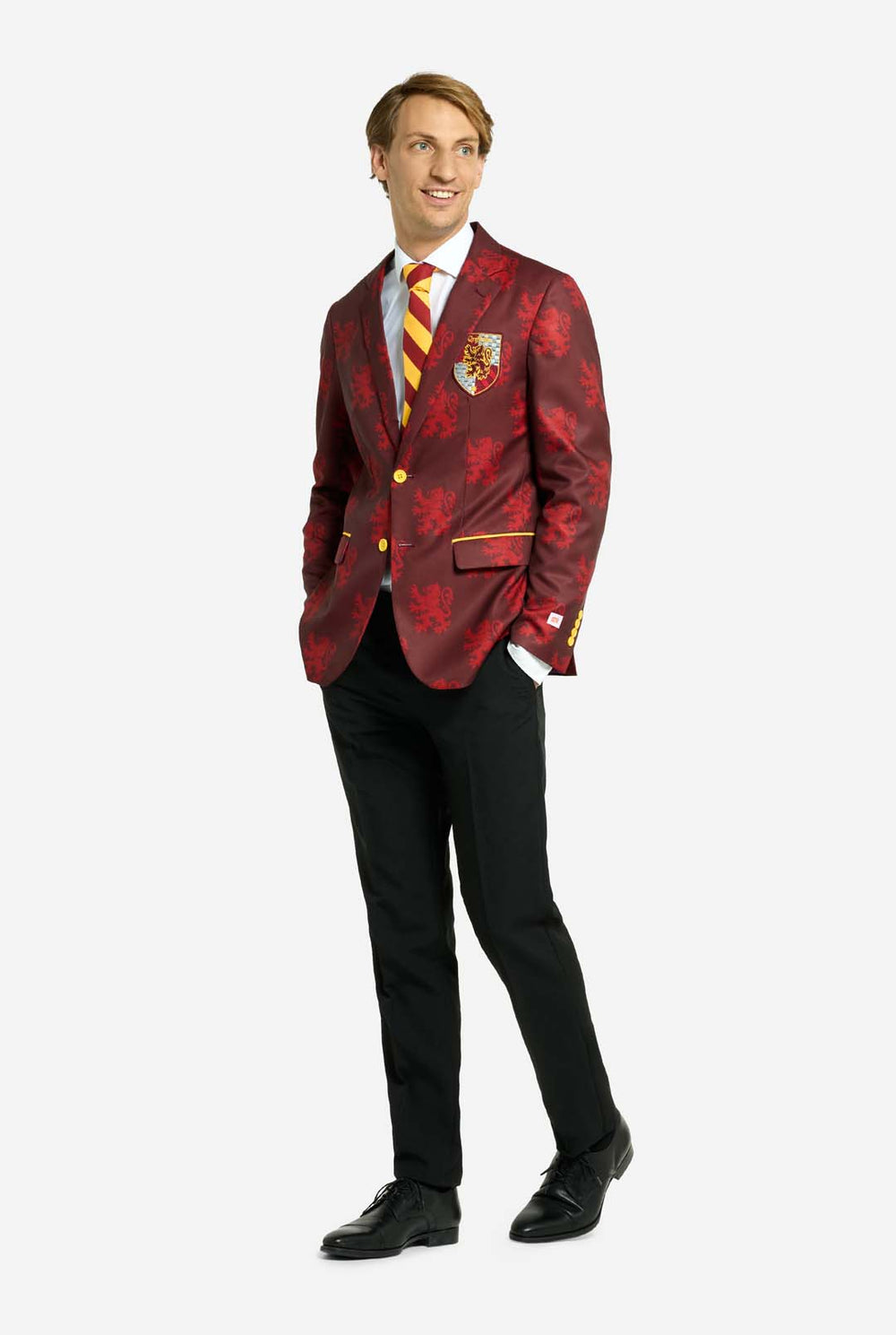 Bild mit hellgrauem Hintergrund und einem Mann, der einen Harry-Potter-Anzug im Gryffindor-Stil trägt. Der Anzug besteht aus einem roten Blazer mit Gryffindor-Logo und hellrotem Löwen-Allover-Print, schwarzen Hosen und einer rot-gelb diagonal gestreiften Krawatte.