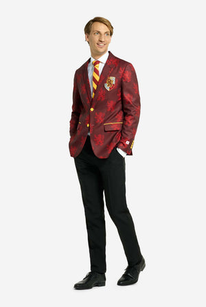 Bild mit hellgrauem Hintergrund und einem Mann, der einen Harry-Potter-Anzug im Gryffindor-Stil trägt. Der Anzug besteht aus einem roten Blazer mit Gryffindor-Logo und hellrotem Löwen-Allover-Print, schwarzen Hosen und einer rot-gelb diagonal gestreiften Krawatte. Der Mann hat die Hände in den Taschen und schaut seitlich weg.