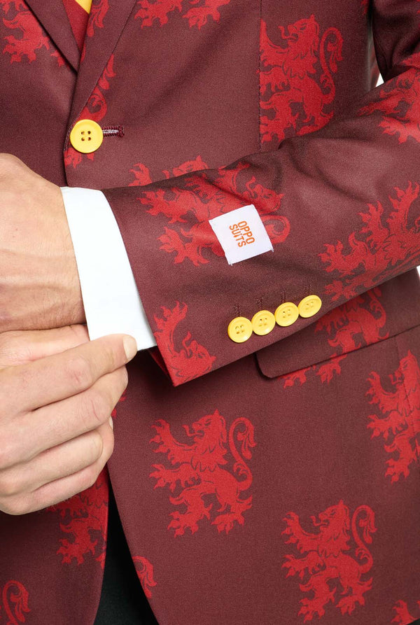 Bild mit hellgrauem Hintergrund und einem Mann, der einen Harry-Potter-Anzug im Gryffindor-Stil trägt. Der Anzug besteht aus einem roten Blazer mit Gryffindor-Logo und einem hellroten Löwen-Allover-Print, schwarzen Hosen und einer rot-gelb diagonal gestreiften Krawatte. Nahaufnahme des Ärmels.