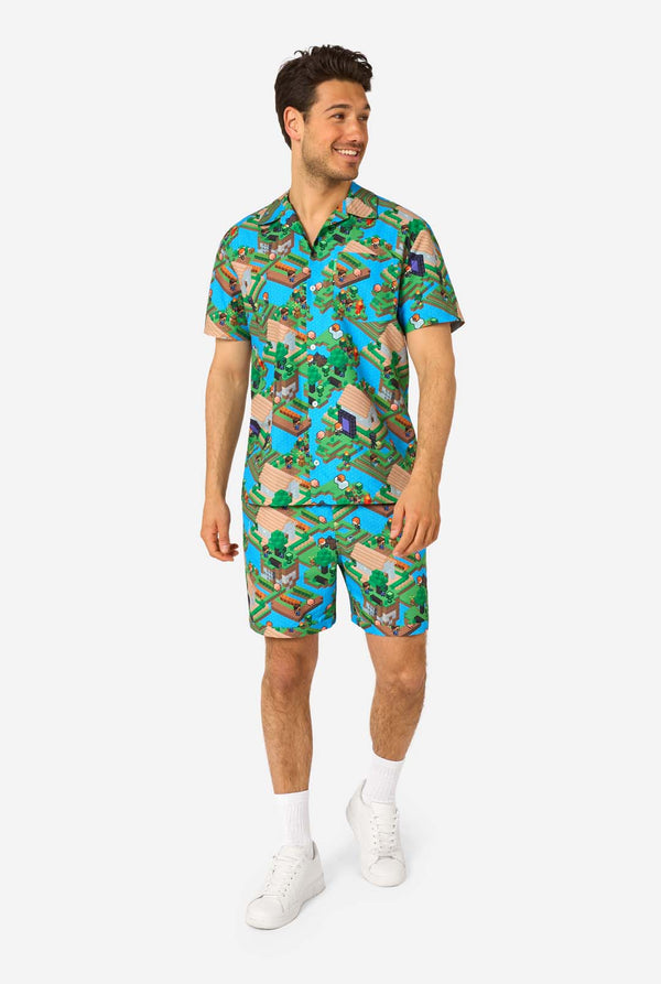 Ein Mann trägt ein buntes Sommeroutfit mit einem Minecraft-Overworld-Motiv, das pixelige Landschaften, Charaktere und Elemente aus dem ikonischen Spiel zeigt. Das kurzärmelige Hemd und die passenden Shorts heben ein lebhaftes Design hervor, das von der Minecraft-Welt inspiriert ist. Ganzkörperbild.