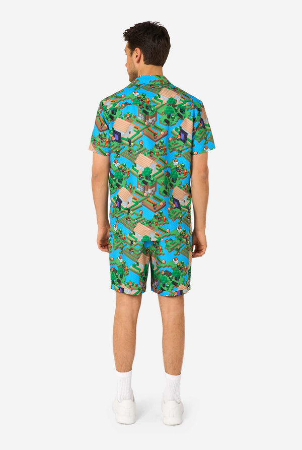 Ein Mann trägt ein buntes Sommeroutfit mit einem Minecraft-Overworld-Motiv, das pixelige Landschaften, Charaktere und Elemente aus dem ikonischen Spiel zeigt. Das kurzärmelige Hemd und die passenden Shorts heben ein lebhaftes Design hervor, das von der Minecraft-Welt inspiriert ist. Ansicht von hinten.