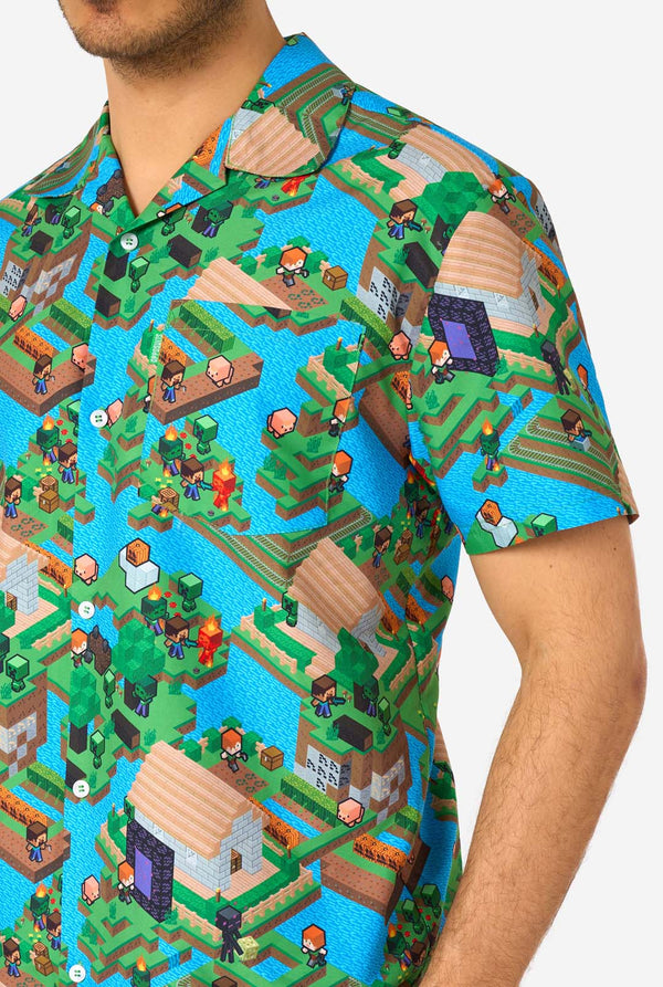 Ein Mann trägt ein buntes Sommeroutfit mit einem Minecraft-Overworld-Motiv, das pixelige Landschaften, Charaktere und Elemente aus dem ikonischen Spiel zeigt. Das kurzärmelige Hemd und die passenden Shorts heben ein lebhaftes Design hervor, das von der Minecraft-Welt inspiriert ist. Nahaufnahme der Brust.