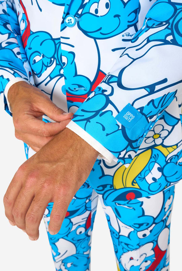 Mann trägt einen farbenfrohen Schlümpfe-Herrenanzug mit durchgehendem Cartoon-Print in Blau, Weiß, Rot und Gelb, inklusive passender Krawatte und weißem Hemd, stehend vor einem schlichten Hintergrund. Nahaufnahme des Ärmels.
