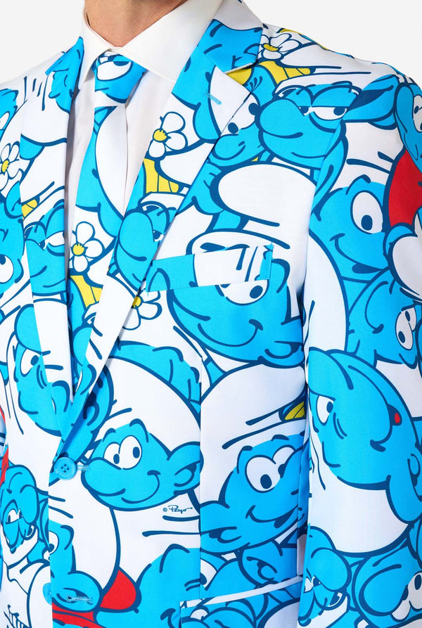 Mann trägt einen farbenfrohen Schlümpfe-Herrenanzug mit durchgehendem Cartoon-Print in Blau, Weiß, Rot und Gelb, inklusive passender Krawatte und weißem Hemd, stehend vor einem schlichten Hintergrund. Nahaufnahme des Oberkörpers.