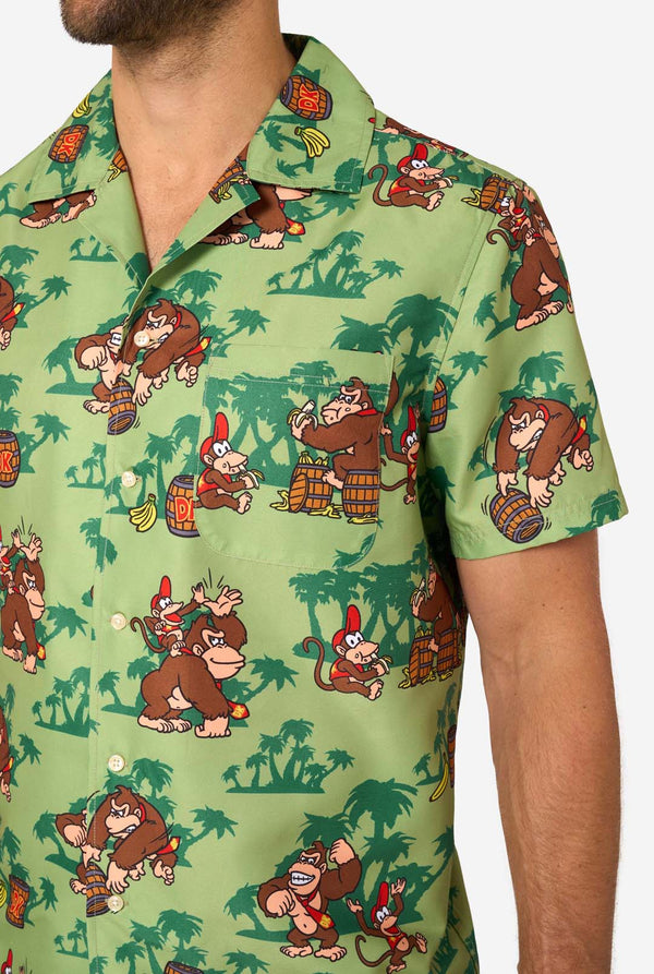 Bild eines Mannes, der ein Hawaiihemd mit Donkey-Kong-Motiv trägt. Das T-Shirt hat einen hellgrünen Hintergrund und enthält dunkelgrüne Palmen sowie mehrere Bilder der Figur Donkey Kong aus Super Mario. Nahaufnahme der Brust.