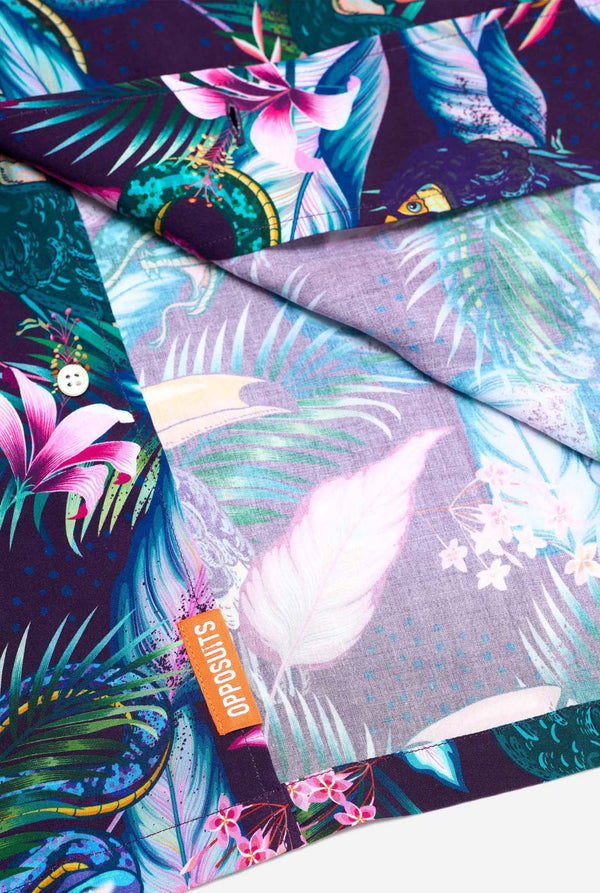 Das Bild zeigt ein lila Hawaiihemd mit tropischem Print, der an die Dschungelnacht erinnert. Der Print besteht aus Papageien, Schlangen, Blättern und Blumen. Nahaufnahme.