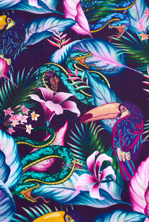 Das Bild zeigt ein lila Hawaiihemd mit tropischem Print, der an das Nachtleben im Dschungel erinnert. Der Print besteht aus Papageien, Schlangen, Blättern und Blumen. Nahaufnahme.