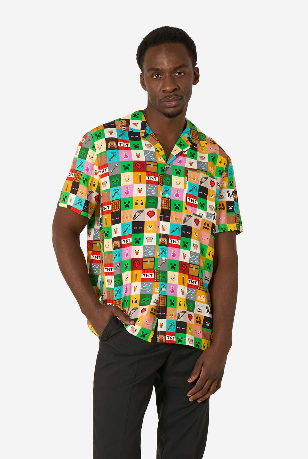 Mann, der ein farbenfrohes Minecraft-Hawaiihemd mit pixeligen Blöcken, Charakteren und Gegenständen aus dem Spiel trägt, gepaart mit einer schwarzen Hose, steht vor einem schlichten weißen Hintergrund.