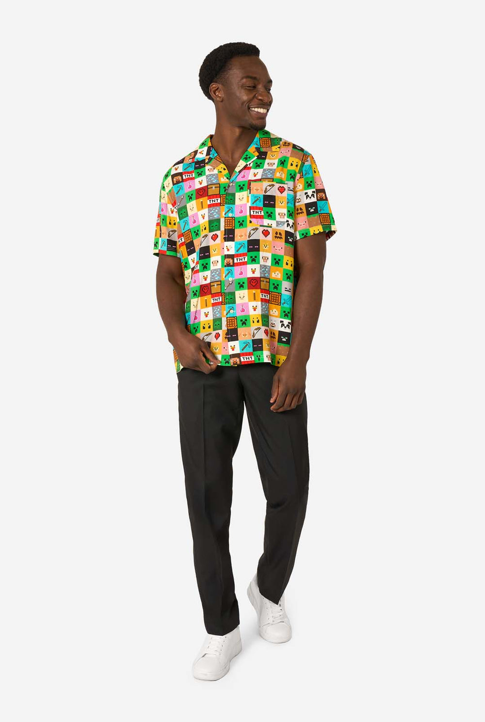 Mann, der ein farbenfrohes Minecraft-Hawaiihemd mit pixeligen Blöcken, Charakteren und Gegenständen aus dem Spiel trägt, gepaart mit einer schwarzen Hose, steht vor einem schlichten weißen Hintergrund.