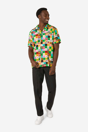 Mann, der ein farbenfrohes Minecraft-Hawaiihemd mit pixeligen Blöcken, Charakteren und Gegenständen aus dem Spiel trägt, gepaart mit einer schwarzen Hose, steht vor einem schlichten weißen Hintergrund. Ganzkörperbild