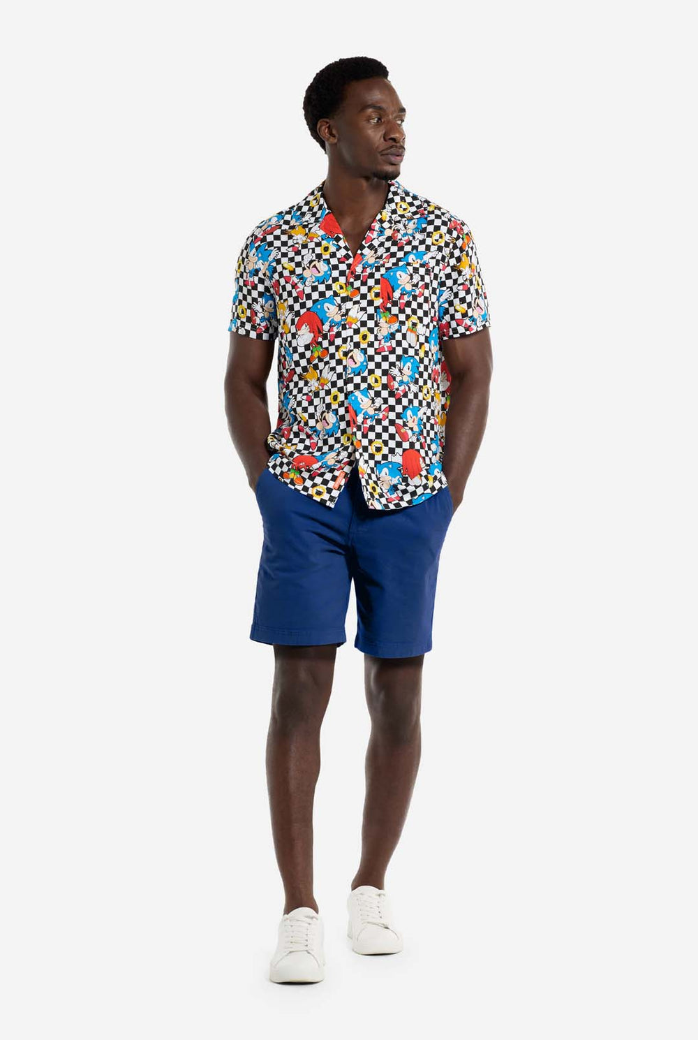 Ein Mann trägt ein schwarz-weiß kariertes Hawaiihemd mit Figuren aus der Sonic the Hedgehog-Reihe und goldenen Ringen darauf. Er lächelt in die Kamera.