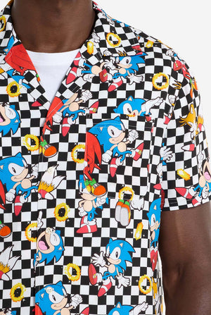 Ein Mann trägt ein schwarz-weiß kariertes Hawaiihemd mit Figuren aus der Sonic the Hedgehog-Reihe und goldenen Ringen darauf. Nahaufnahme der Brust.