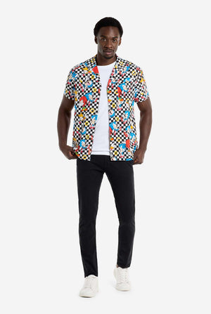 Ein Mann trägt ein schwarz-weiß kariertes Hawaiihemd mit Figuren aus der Sonic the Hedgehog-Reihe und goldenen Ringen. Dazu trägt er eine schwarze Hose. Er blickt in die Kamera und hält den unteren Teil des Hemdes fest.