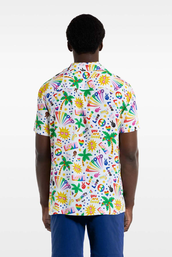 Ein Mann trägt ein weißes Hawaii-Hemd mit einem Regenbogen-Pride-Aufdruck. Der Aufdruck besteht aus Friedenssymbolen, Herzen und anderen Symbolen. Er trägt außerdem eine blaue Hose. Er lächelt in die Kamera und hält sich an den Seiten des Hemdes fest. Ansicht von hinten.