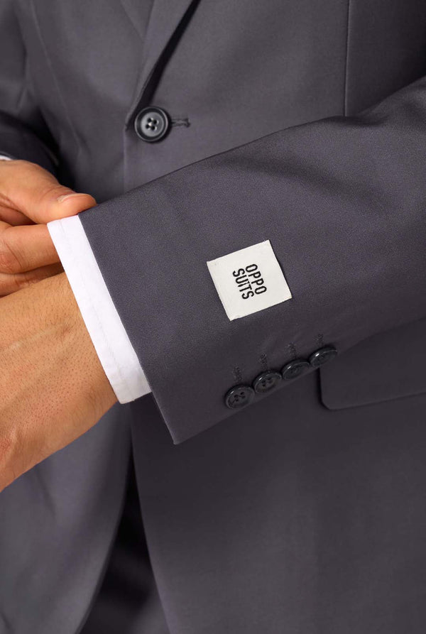 Ein Mann trägt einen stilvollen, anthrazitfarbenen Anzug mit weißem Hemd und wirkt selbstbewusst. Das perfekte formelle Outfit für besondere Anlässe, Hochzeiten und Partys.