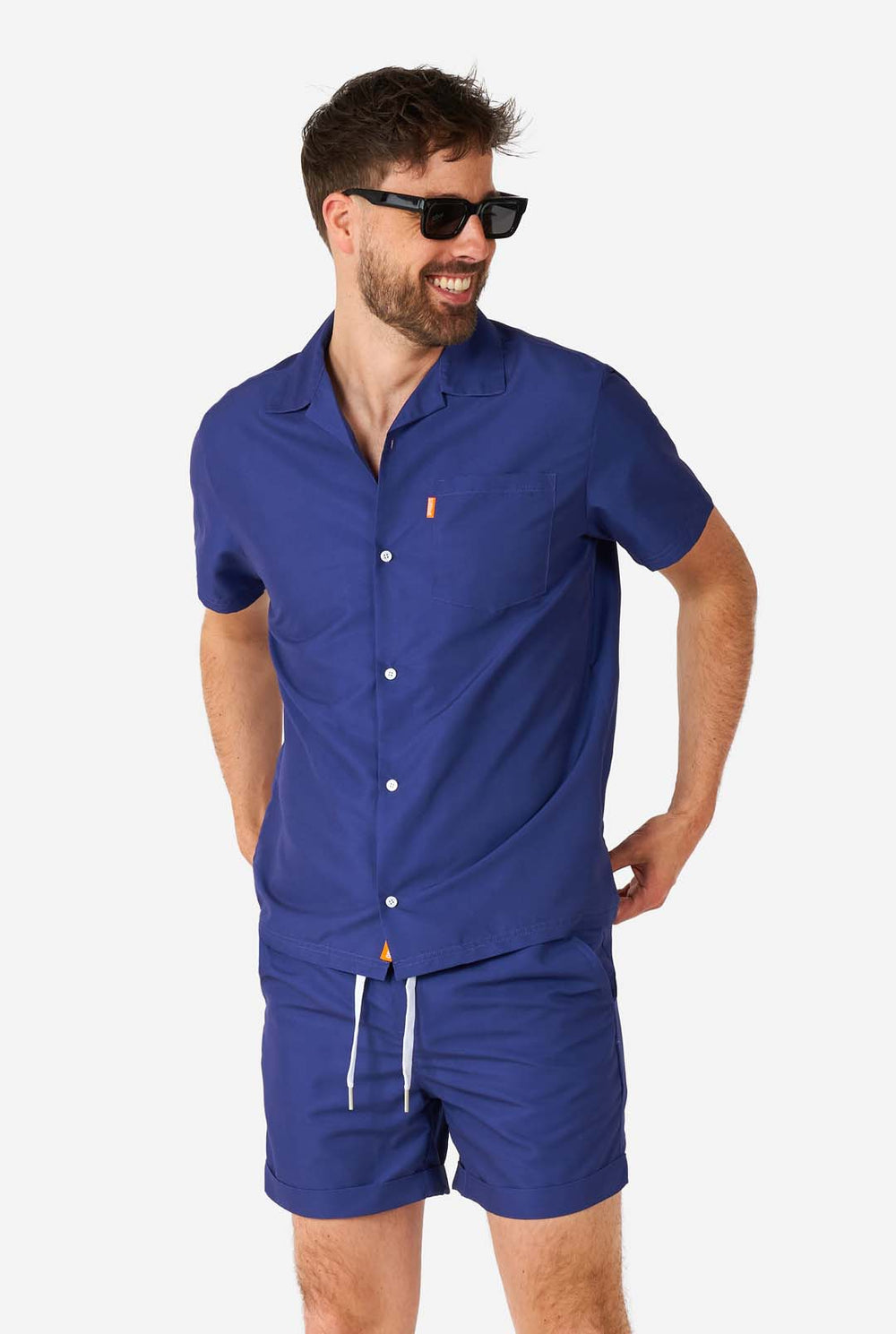 Mann trägt blaues Sommerset bestehend aus Hemd und Shorts und Sonnenbrille.