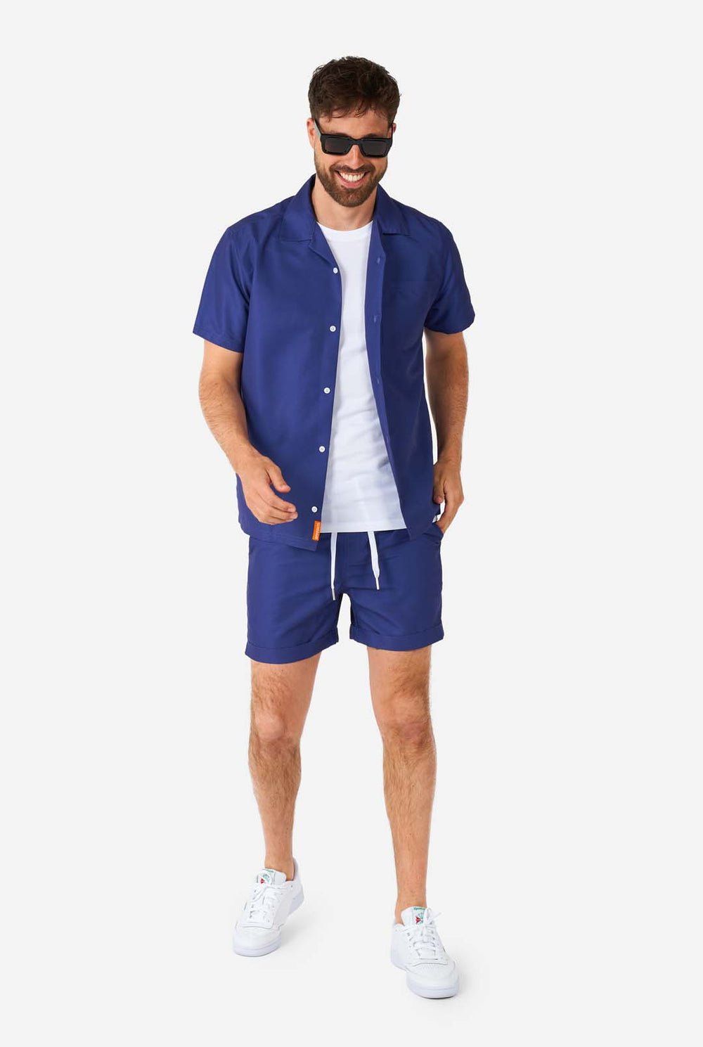 Mann trägt blaues Sommerset bestehend aus Hemd und Shorts und Sonnenbrille.