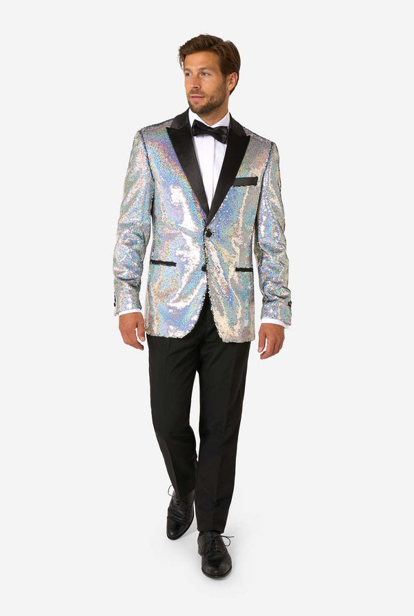 Mann, der einen holographischen silbernen Paillettentuxedo mit schwarzen Satin -Repfels trägt, gepaart mit einem weißen Hemd, einer schwarzen Fliege und einer schwarzen Hose.