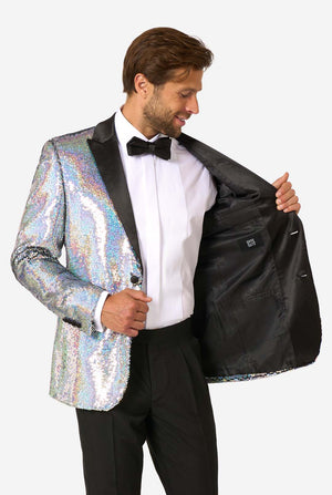 Mann, der einen holographischen silbernen Paillettentuxedo mit schwarzen Satin -Repfels trägt, gepaart mit einem weißen Hemd, einer schwarzen Fliege und einer schwarzen Hose.