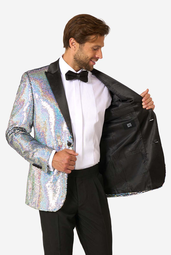 Mann, der einen holographischen silbernen Paillettentuxedo mit schwarzen Satin -Repfels trägt, gepaart mit einem weißen Hemd, einer schwarzen Fliege und einer schwarzen Hose.