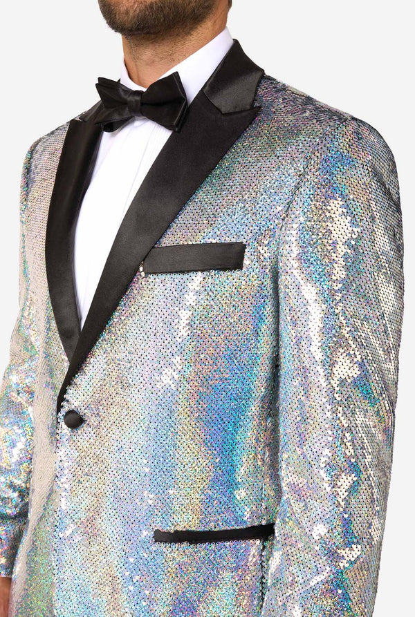 Mann, der einen holographischen silbernen Paillettentuxedo mit schwarzen Satin -Repfels trägt, gepaart mit einem weißen Hemd, einer schwarzen Fliege und einer schwarzen Hose.