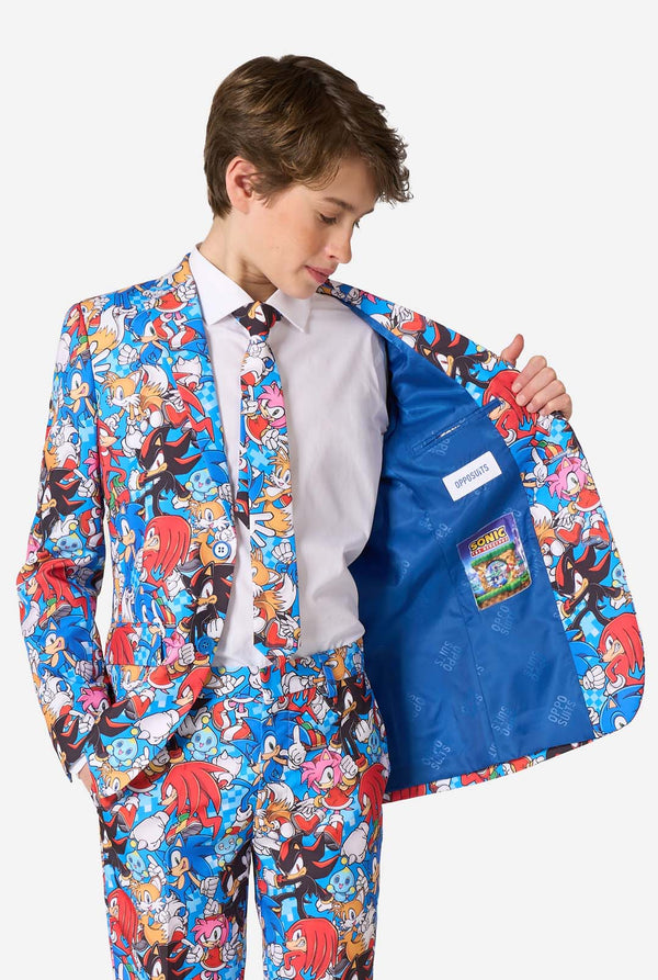 Teenager-Junge in einem farbenfrohen Sonic-Teenie-Anzug mit bunten Aufdrucken von Sonic the Hedgehog-Figuren wie Sonic, Knuckles, Tails und Amy, gepaart mit einer passenden Krawatte und einem weißen Hemd. Er hält eine Seite der Jacke offen.