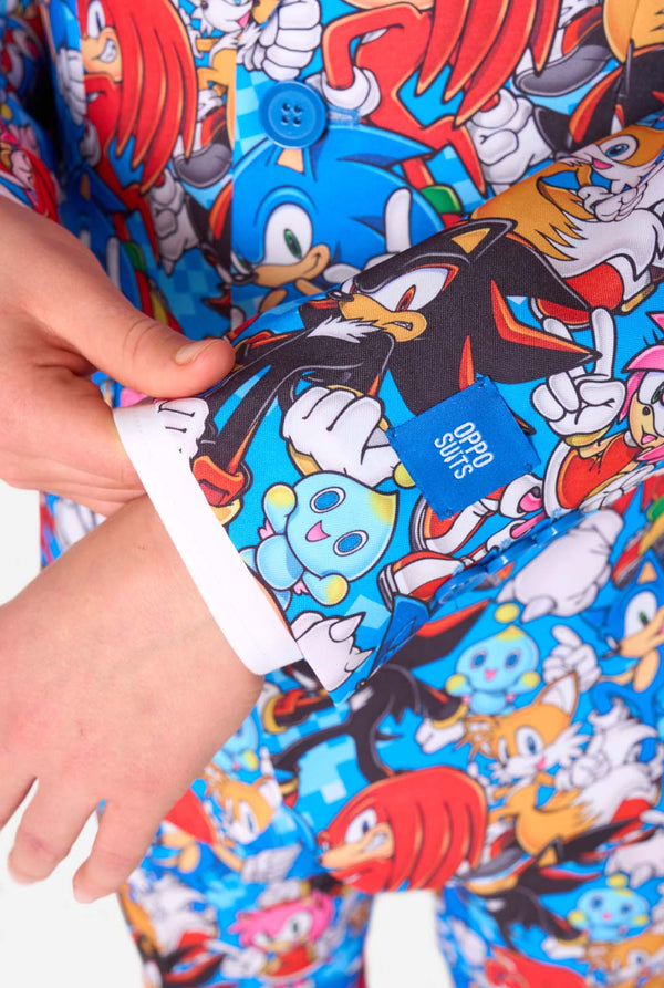 Teenager trägt einen farbenfrohen Sonic-Teenie-Anzug mit bunten Aufdrucken von Sonic the Hedgehog-Figuren wie Sonic, Knuckles, Tails und Amy, gepaart mit einer passenden Krawatte und einem weißen Hemd. Nahaufnahme des Ärmels.