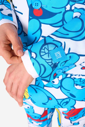 Jugendlicher Junge trägt einen lebendigen Schlümpfe-Kinderanzug mit farbenfrohen Cartoon-Motiven in Blau, Rot, Gelb und Weiß, kombiniert mit passender Krawatte und weißem Hemd, lächelt vor einem schlichten Hintergrund. Nahaufnahme des Ärmels.