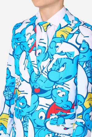 Jugendlicher Junge trägt einen auffälligen Kindersmoking mit Schlümpfe-Motiv und bunten Cartoon-Prints in Blau, Rot, Gelb und Weiß, kombiniert mit passender Krawatte und weißem Hemd, lächelt vor neutralem Hintergrund. Nahaufnahme des Oberkörpers.