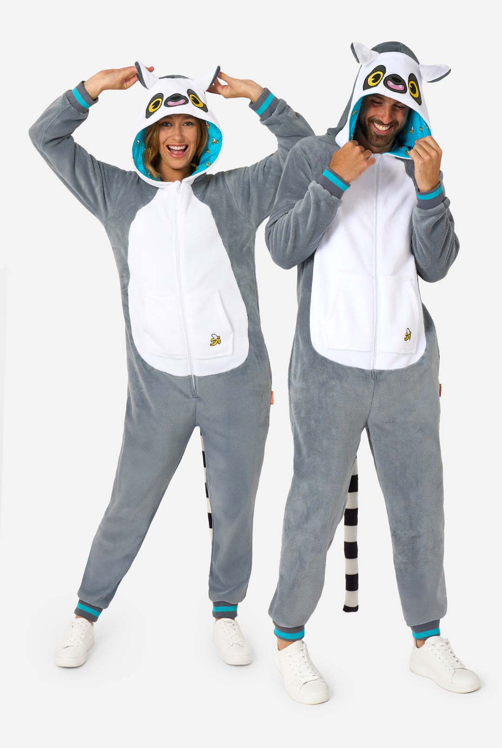 Ein Mann und eine Frau tragen einen grau-weißen Lemur-Onesie für Erwachsene mit verspielten Kapuzendetails und kuschelig weichem Material, perfekt zum Faulenzen oder für Kostümveranstaltungen. Mit schwarzem und weißem Schwanz. Die Kapuze ist auf dem Kopf.