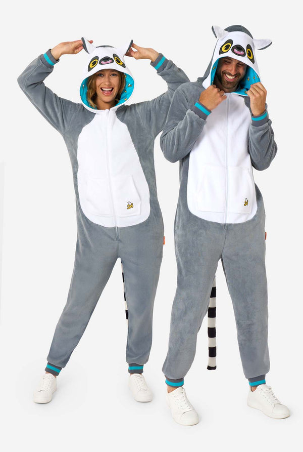 Ein Mann und eine Frau tragen einen grau-weißen Lemur-Onesie für Erwachsene mit verspielten Kapuzendetails und kuschelig weichem Material, perfekt zum Faulenzen oder für Kostümveranstaltungen. Mit schwarzem und weißem Schwanz. Die Kapuze haben sie auf dem Kopf. Ganzkörperbild.