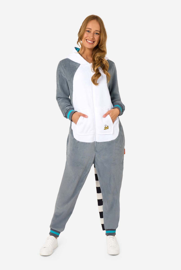 Eine Frau trägt einen grau-weißen Lemur-Onesie für Erwachsene mit verspielten Kapuzendetails und kuschelig weichem Material, perfekt zum Faulenzen oder für Kostümveranstaltungen. Mit schwarzem und weißem Schwanz. Die Kapuze befindet sich auf ihrem Rücken. Ganzkörperabbildung.