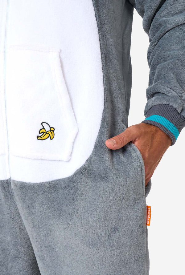Ein Mann trägt einen grau-weißen Lemuren-Onesie für Erwachsene mit verspielten Kapuzendetails und kuscheligem, weichem Material, perfekt zum Entspannen oder für Kostümveranstaltungen. Inklusive schwarz-weißem Schwanz. Nahaufnahme der Tasche.