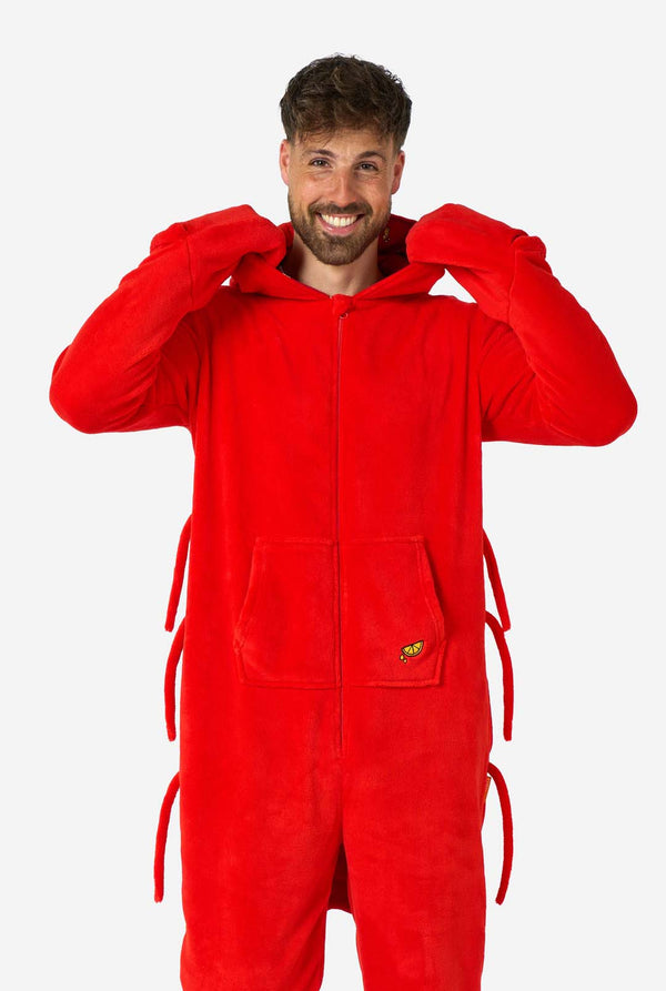 Ein Mann trägt einen leuchtend roten Onesie für Erwachsene mit Hummermotiv, verspielten Kapuzendetails und kuscheligem, weichem Material, perfekt zum Entspannen oder für Kostümveranstaltungen. Mit aufgenähten Handschuhen als Krallen. Die Kapuze ist auf seinem Rücken heruntergezogen.