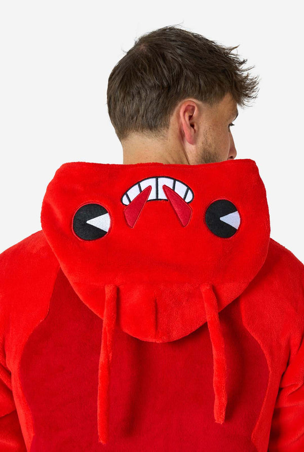 Ein Mann trägt einen leuchtend roten Onesie mit Hummermotiv für Erwachsene mit verspielten Kapuzendetails und kuscheligem, weichem Material – perfekt zum Entspannen oder für Kostümpartys. Mit aufgenähten Handschuhen als Krallen. Nahaufnahme von der Kapuze auf seinem Rücken.