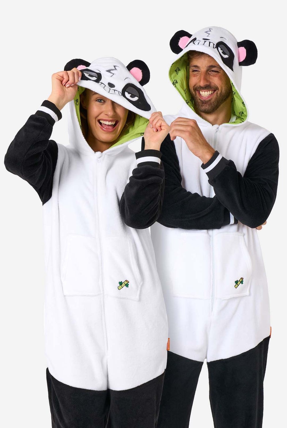 Ein Mann und eine Frau tragen panda-motivierte Erwachsenen-Onesies. Diese gemütlichen Onesies zeigen die typischen schwarz-weißen Pandafarben und eine verspielte Kapuze mit Panda-Ohren und einem niedlichen Gesicht. Perfekt zum Entspannen oder für lustige Kostüm-Anlässe.