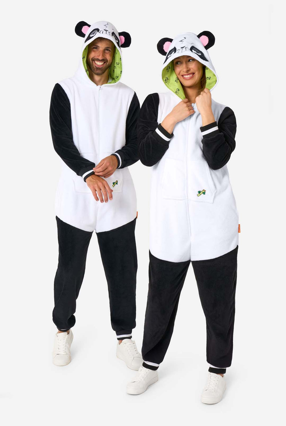 Ein Mann und eine Frau tragen panda-motivierte Erwachsenen-Onesies. Diese gemütlichen Onesies zeigen die typischen schwarz-weißen Pandafarben und eine verspielte Kapuze mit Panda-Ohren und einem niedlichen Gesicht. Perfekt zum Entspannen oder für lustige Kostüm-Anlässe.
