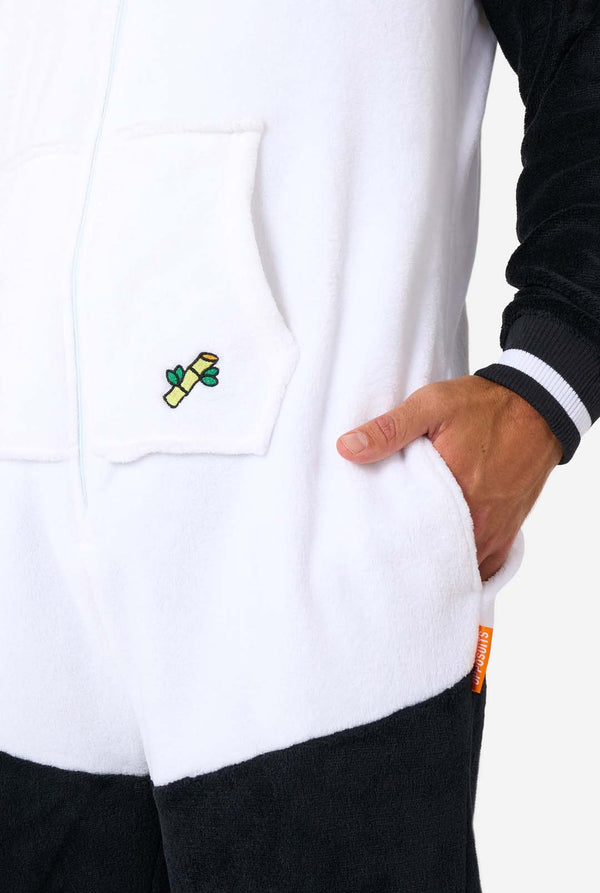Ein Mann trägt einen Panda-Onesie für Erwachsene. Dieser kuschelige Onesie ist in den Farben Schwarz und Weiß gehalten und hat eine verspielte Kapuze mit Panda-Ohren und einem süßen Gesicht. Perfekt zum Entspannen oder für lustige Kostümanlässe. Nahaufnahme der Tasche.