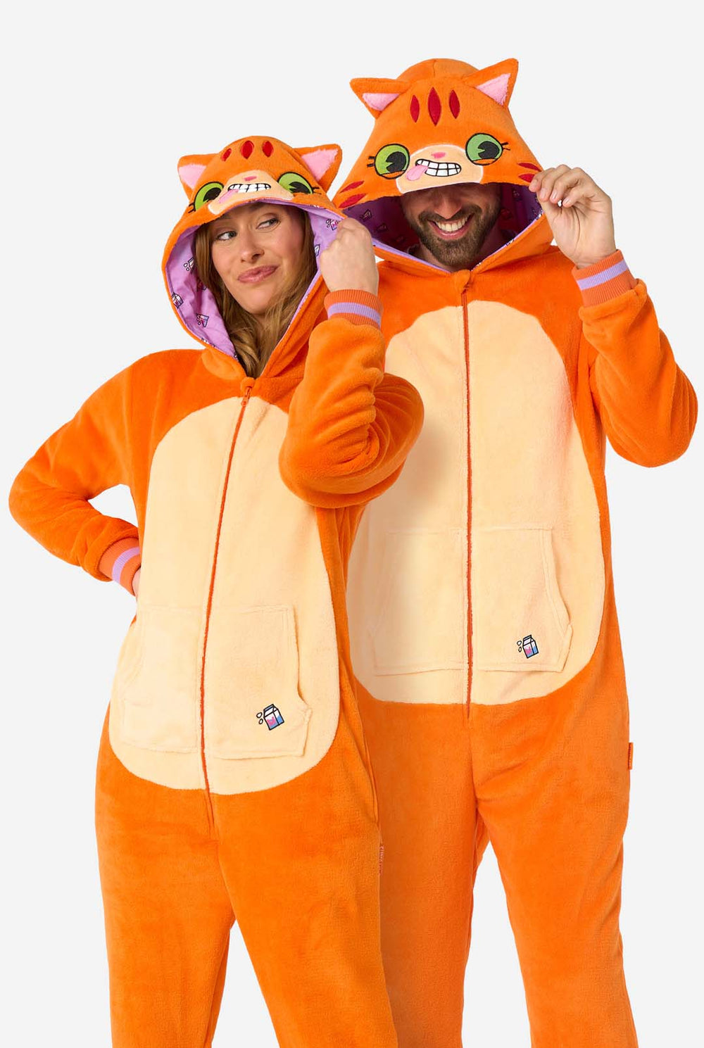 Ein Mann und eine Frau tragen einen orangefarbenen Strampler für Erwachsene in Form eines roten Katzen-Stramplers. Der Strampler hat eine Kapuze, die einem Katzenkopf ähnelt, und Katzendetails, perfekt für gemütliches Faulenzen oder Kostümpartys. Beide haben die Kapuze auf dem Kopf.