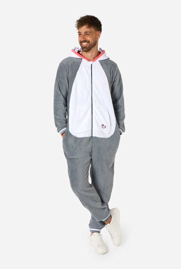 Ein Mann trägt einen grau-weißen Hai-Onesie für Erwachsene mit verspielten Kapuzendetails und kuscheligem, weichem Material, perfekt zum Entspannen oder für Kostümveranstaltungen. Ganzkörperbild und zwei Hände in den Taschen.