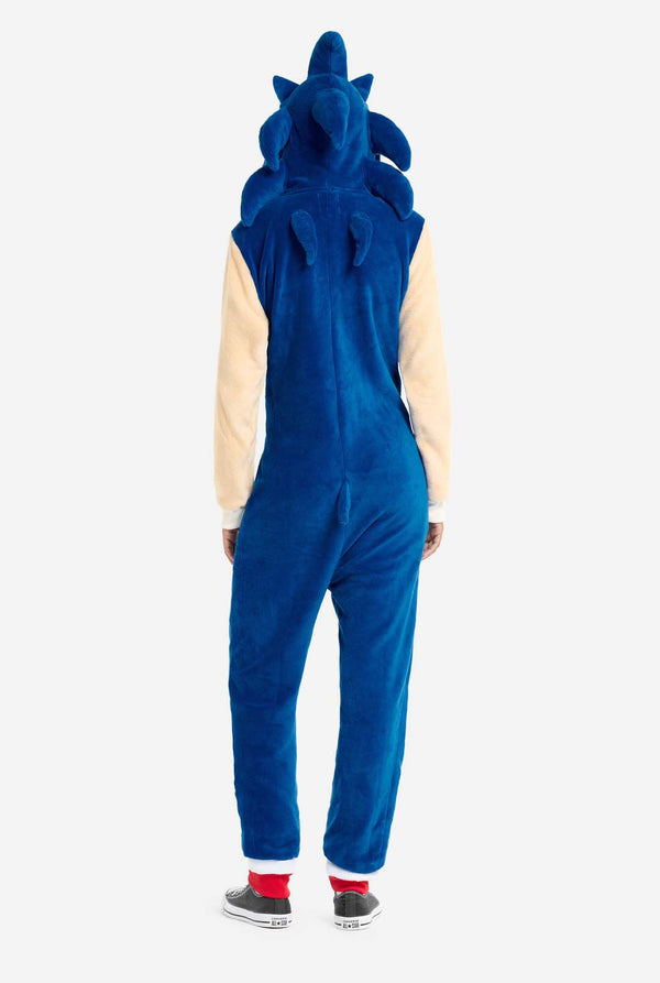 Eine Frau trägt einen kuscheligen, blauen Sonic the Hedgehog-Einteiler für Erwachsene mit weichen, beigen Ärmeln, die Sonics ikonischen Look nachahmen. Die Kapuze des Einteilers ist mit Sonics erkennbarem Gesicht gestaltet, einschließlich großer grüner Augen, blauer Stacheln und spitzer Ohren. Dieser Sonic the Hedgehog-Einteiler ist ideal für Cosplay, zum Entspannen oder für Themenveranstaltungen. Ansicht von hinten.