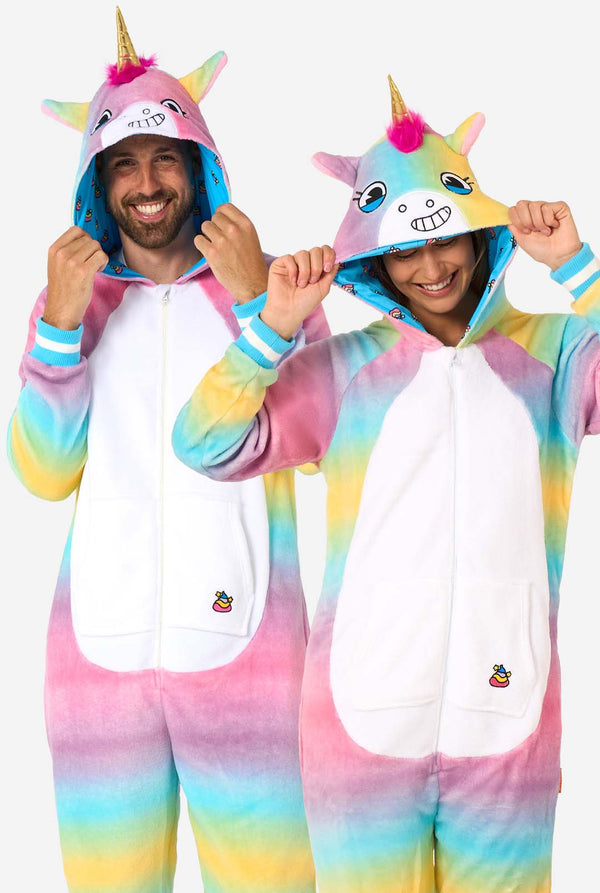 Ein Mann und eine Frau tragen einen farbenfrohen Strampler für Erwachsene in Form eines Regenbogen-Einhorns. Der Strampler hat einen leuchtenden Farbverlauf in Pastellfarben, ein goldenes Horn und verspielte Einhorn-Details - perfekt zum gemütlichen Faulenzen oder für Kostümpartys. Sowohl die Männer als auch die Frauen haben ihre Kapuze auf.
