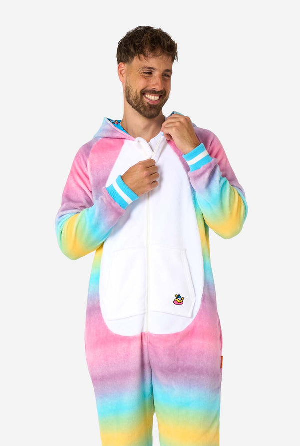 Ein Mann trägt einen farbenfrohen Einteiler für Erwachsene in Form eines Regenbogen-Einhorns. Der Einteiler besticht durch einen leuchtenden Farbverlauf in Pastellfarben, ein goldenes Horn und verspielte Einhorn-Details – perfekt für gemütliches Faulenzen oder Kostümpartys. Die Kapuze liegt flach auf seinem Rücken.