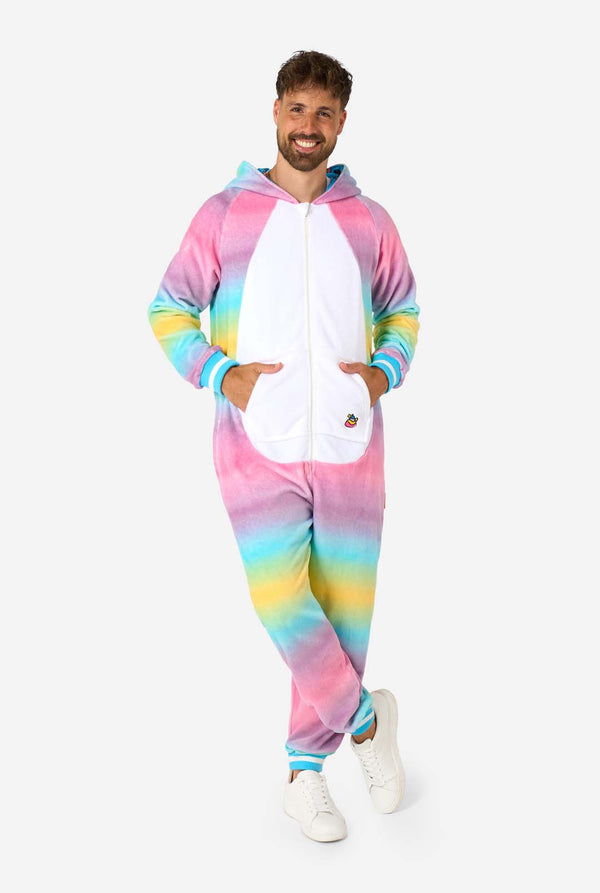 Ein Mann trägt einen farbenfrohen Einteiler für Erwachsene in Form eines Regenbogen-Einhorns. Der Einteiler besticht durch einen leuchtenden Farbverlauf in Pastellfarben, ein goldenes Horn und verspielte Einhorn-Details – perfekt für gemütliches Faulenzen oder Kostümpartys. Die Kapuze liegt flach auf seinem Rücken. Ganzkörperbild.