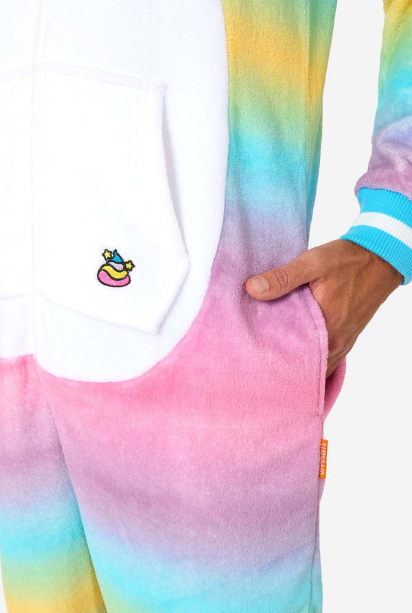 Ein Mann trägt einen farbenfrohen Einteiler für Erwachsene in Form eines Regenbogen-Einhorns. Der Einteiler besticht durch einen leuchtenden Farbverlauf in Pastellfarben, ein goldenes Horn und verspielte Einhorn-Details. Nahaufnahme der Tasche.